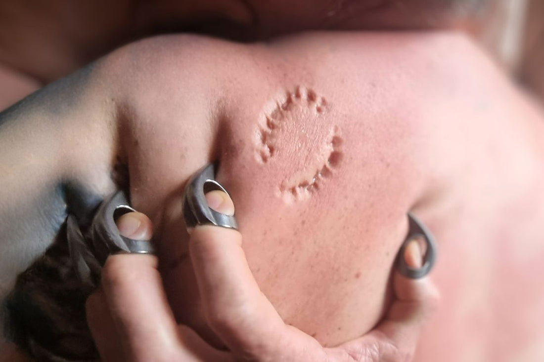 Hand wearing Metal BDSM finger Claws during Primal Play. Claws are sunk into bare skin showing a large bite mark into the flesh of the shoulder