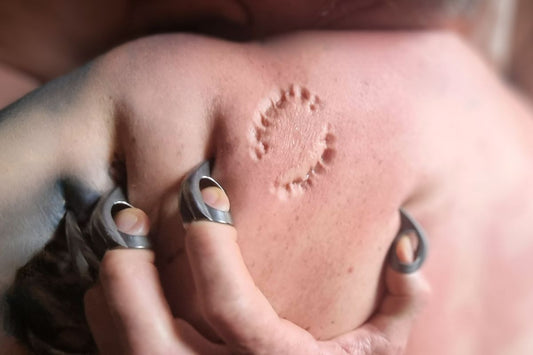 Hand wearing Metal BDSM finger Claws during Primal Play. Claws are sunk into bare skin showing a large bite mark into the flesh of the shoulder