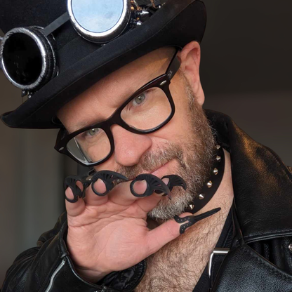 Handsmoe man wearing a steampunk top hat with goggles brandishes bold black finger Claws with intricate detailing.
